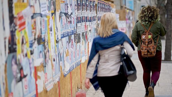 Женщины идут по улице вдоль забора, на  котором наклеены предвыборные плакаты - Sputnik Грузия