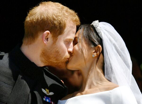 Принц Гарри и Меган Маркл целуются на ступеньках часовни Святого Георгия после свадебной церемонии. Бабушка принца, королева Великобритании Елизавета Вторая пожаловала принцу Гарри титул герцога Сассекского, его супруга отныне будет именоваться герцогиней Сассекской - Sputnik Грузия