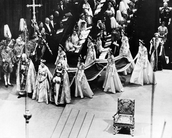 Король Георг VI, отец Елизаветы, умер 6 февраля 1952 года. 8 февраля 1952 года, сопровождаемая своим супругом Филиппом, Елизавета приняла присягу Тайного совета и подписала клятву престолонаследия. Час спустя герольдмейстер официально объявил о её вступлении на престол с балкона Сент-Джеймсского дворца. С последними его словами Боже, храни королеву!, все флаги Лондона, приспущенные после смерти короля, одновременно поднялись вверх в честь новой королевы Великобритании. На фото - Королева Елизавета II идет к алтарю во время церемонии коронации - Sputnik Грузия