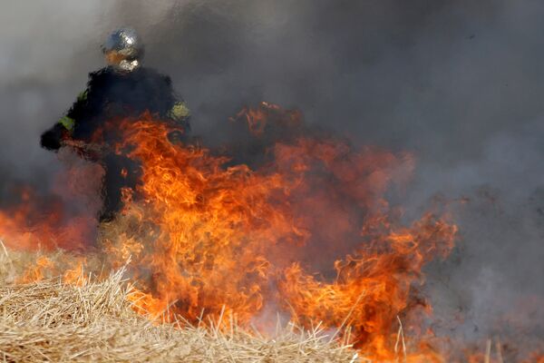 Французский пожарный использует лопату для борьбы с пламенем в горящем поле ячменя во время сезона сбора урожая в Ниарни, Франция - Sputnik Грузия
