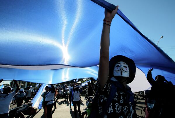 Демонстрант в маске держит большой государственный флаг во время протеста против президента Никарагуа Даниэля Ортеги в Манагуа - Sputnik Грузия