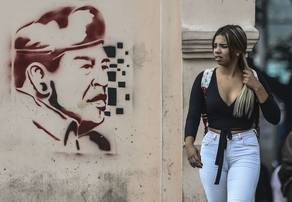 Женщина проходит мимо изображения бывшего президента Венесуэлы Уго Чавеса в Каракасе - Sputnik Грузия