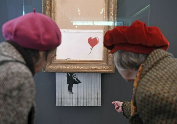 Посетители смотрят на самоуничтожившуюся после продажи на аукционе картину художника Бэнкси Девочка с воздушным шаром, которая теперь называется Любовь в мусорном баке, в Музее современного искусства в Баден-Бадене - Sputnik Грузия