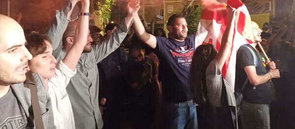 Митингующие, взявшись за руки, выстроились в живую цепь на фоне горящих файеров. Акция протеста в столице Грузии - Sputnik Грузия
