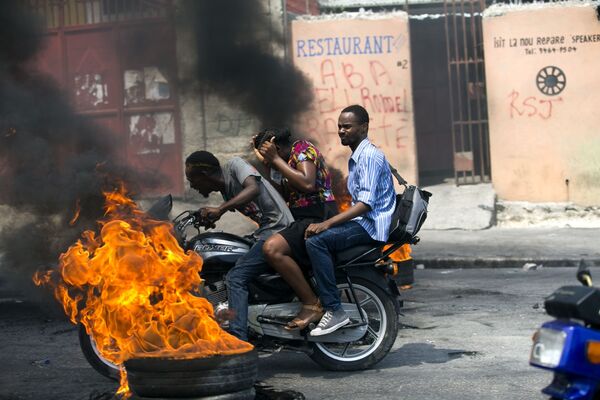Мототакси, проезжающее мимо горящей шины в Порт-о-Пренсе, Гаити - Sputnik Грузия