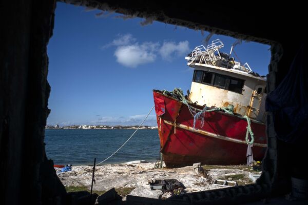 Корабль, севший на мель от ураганного ветра, виден сквозь разрушенную штормом стену дома в Абако - Sputnik Грузия