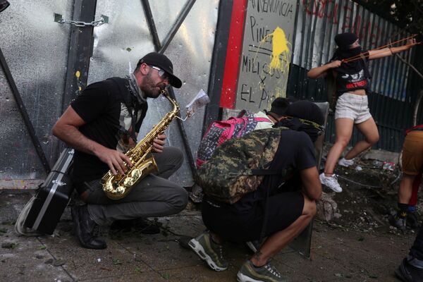 Мужчина играет на саксофоне за демонстрантами, которые принимают участие в акции протеста против правительства в Сантьяго - Sputnik Грузия