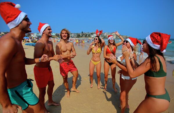 Хоть Австралия и находится на другом конце планеты, там живут бывшие европейцы, которые хранят традицию празднования Нового года. Туристы в рождественских костюмах на пляже в Сиднее - Sputnik Грузия