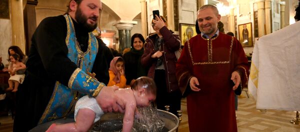 Священник держит в руках ребенка во время церемонии массового крещения детей в храме Самеба - Sputnik Грузия