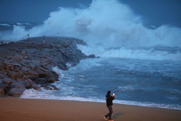 Мужчина фотографирует шторм Глория на пляже Барселонета в Барселоне - Sputnik Грузия