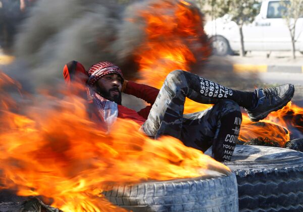 Демонстрант среди горящих шин, блокирующих дорогу во время антиправительственных акций протеста в Наджафе, Ирак - Sputnik Грузия