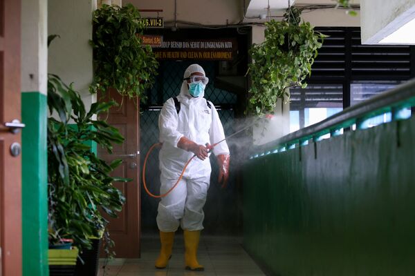 Волонтер из Индонезийского Красного Креста в защитном костюме распыляет дезинфицирующее средство в коридоре школы, закрытой, как и другие учебные заведения, из-за угрозы распространения коронавируса - Sputnik Грузия