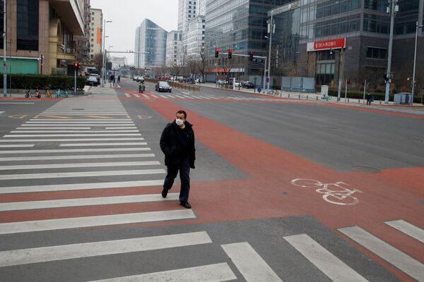 А вот как сегодня выглядит Пекин, где еще несколько месяцев назад все улицы были переполнены в любое время года. На фото - прохожий в маске идет по пустым улицам в центральном деловом районе Пекина - Sputnik Грузия