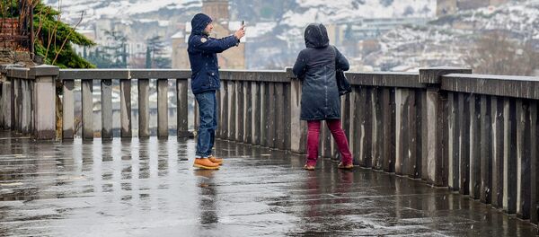 Тбилиси в снегу. Мужчина фотографирует женщину на фоне города - Sputnik Грузия