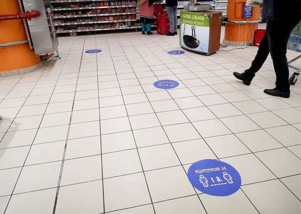 Для того, чтобы люди в супермаркетах и продуктовых магазинах соблюдали дистанцию, на полу стали расклеивать специальные предупреждающие наклейки. Но как видно на фото выше, не все обращают внимание на это и подходят близко друг к другу - Sputnik Грузия