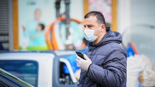 Мужчина с телефоном в маске и перчатках идет по улице. В Грузии борются с коронавирусом - Sputnik Грузия