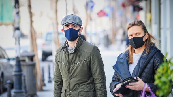 Мужчина в кепке и синей маске и женщина в перчатках и черной маске на улице. В Грузии борются с коронавирусом - Sputnik Грузия