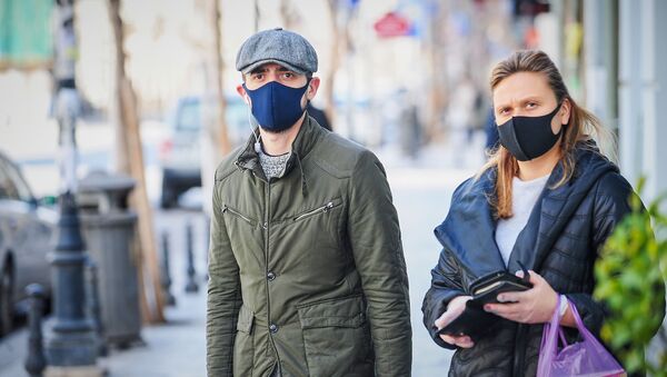 Мужчина в кепке и синей маске и женщина в перчатках и черной маске на улице. В Грузии борются с коронавирусом - Sputnik Грузия
