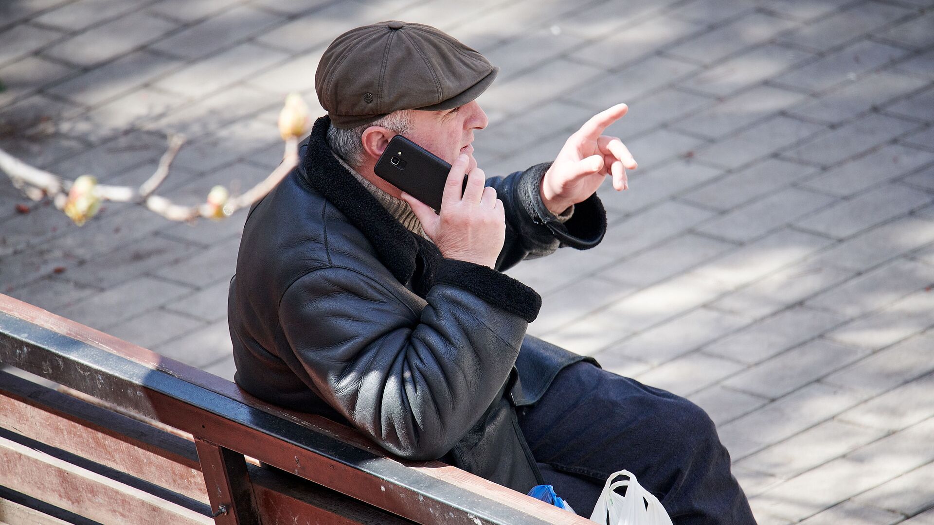 Мужчина сидит на скамейке в парке с покупками из магазина и говорит по телефону. В Грузии введен карантин и принимаются меры по борьбе с коронавирусом - Sputnik Грузия, 1920, 25.04.2021
