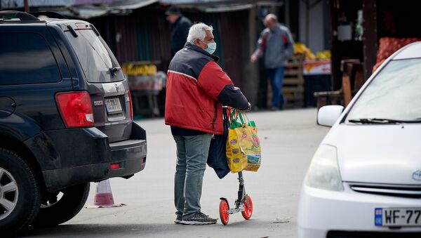 Пожилой мужчина в маске и с самокатом идет по территории рынка - Sputnik Грузия