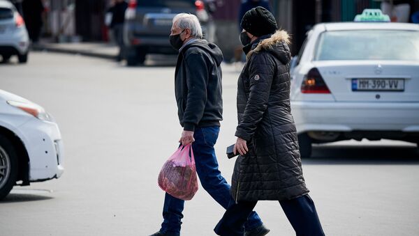 Пожилые муж с женой идут по улице в масках с покупками в руках. В Грузии борются с коронавирусом - Sputnik Грузия