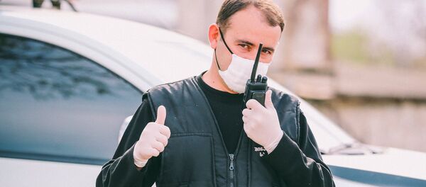 Сотрудник полиции в маске говорит по рации, находясь на посту во время карантина - Sputnik Грузия