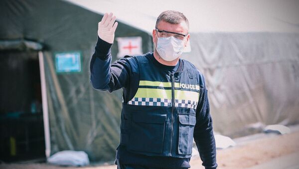 Сотрудник полиции в перчатках и маске на блокпосту у полевого госпиталя - Sputnik Грузия