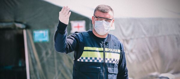 Сотрудник полиции в перчатках и маске на блокпосту у полевого госпиталя - Sputnik Грузия