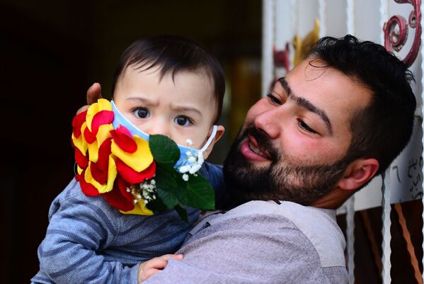 Мужчина с ребенком в украшенной цветами защитной маске в Эн-Наджафе в Ираке - Sputnik Грузия