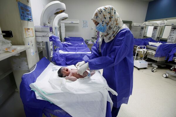 Медсестра в защитной маске и перчатках ухаживает за новорожденным в роддоме в Ираке - Sputnik Грузия