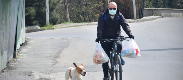Человек в маске едет по городу на велосипеде с продуктами - Sputnik Грузия