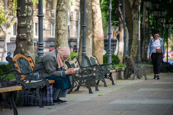 Даже пожилая женщина, сидя на лавочке и читая газету, без маски - Sputnik Грузия