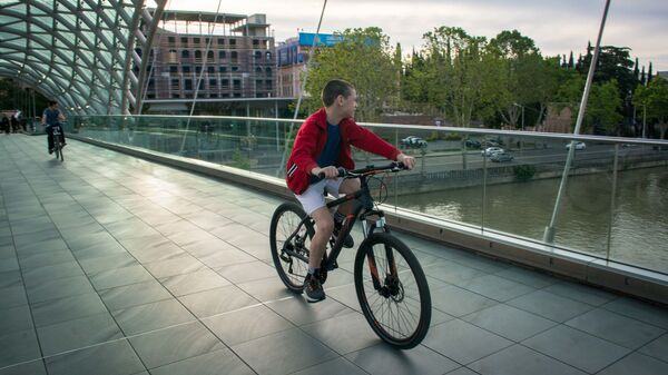 Весна в столице Грузии. Подросток катается на велосипеде по мосту Мира - Sputnik Грузия