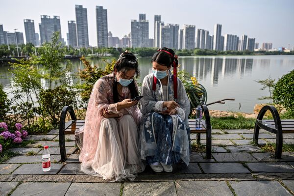 Молодые женщины в масках и в традиционных костюмах на скамейке в парке Уханя в Китае - Sputnik Грузия