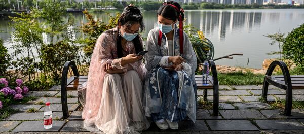 Молодые женщины в масках и в традиционных костюмах на скамейке в парке Уханя, Китай - Sputnik Грузия
