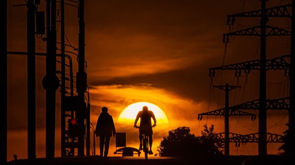 Мужчина едет на велосипеде по одной из улиц в Москве на фоне заката - Sputnik Грузия