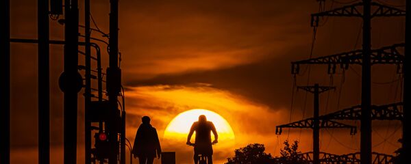 Мужчина едет на велосипеде по одной из улиц в Москве на фоне заката - Sputnik Грузия