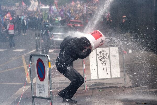 Протестующий прикрывается ведром от удара водяной пушкой, которую полицейские используют для разгона акции протеста медработников во Франции - Sputnik Грузия